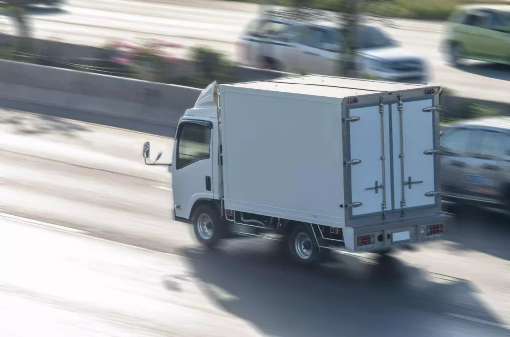 White logistics truck on highway with blurred background, illustrating logistics ROI through improved fleet efficiency and reduced travel time