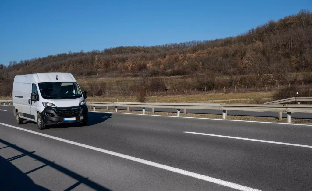 Clean white cargo van cruising past hillside, consistent brand delivery in transit.