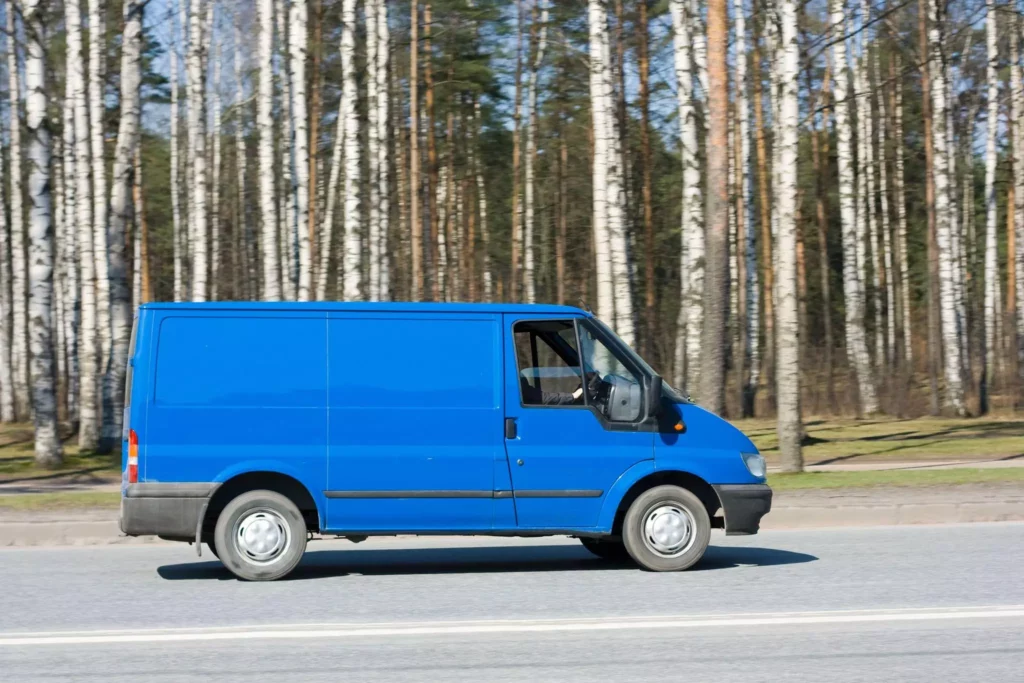 Blue van driving past tall trees in Autumn