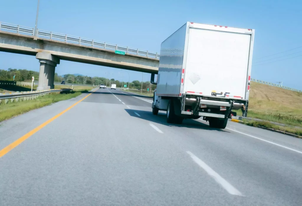 White box truck driving under highway overpass, representing omnichannel logistics and modern customer service expectations.