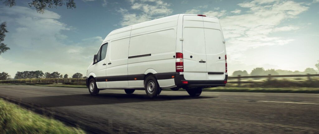 Rear view of long-wheelbase white cargo van on rural highway, signaling predictable delivery windows and sustainability