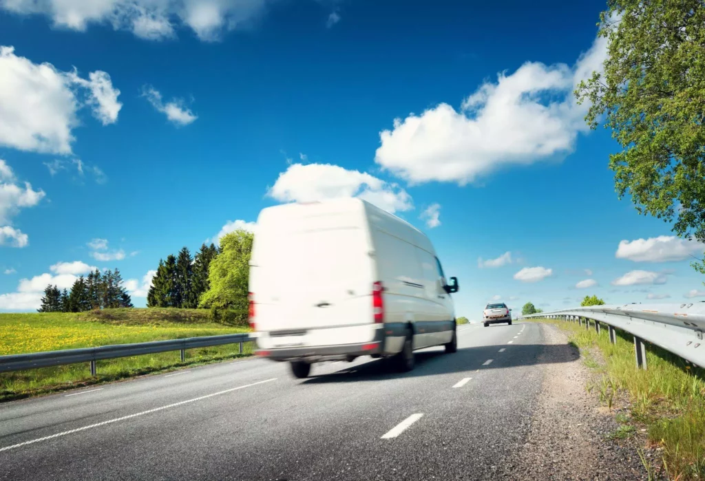 The rear of a white van as it races along a highway on a sunny day