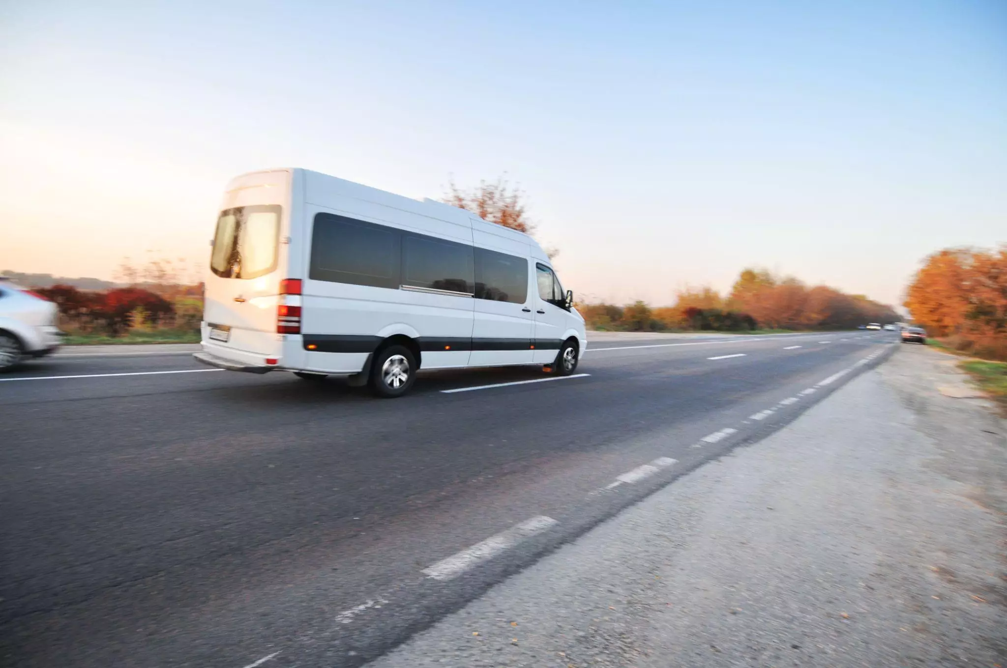 f7c2c2e0-0211-4c43-8788-d7b2f38f28f0 White delivery van accelerating on open road at sunrise, reflecting customer delivery expectations for speed and reliability