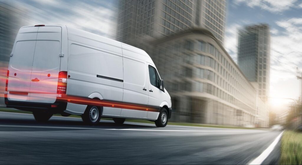 High-roof cargo van speeding past city buildings.
