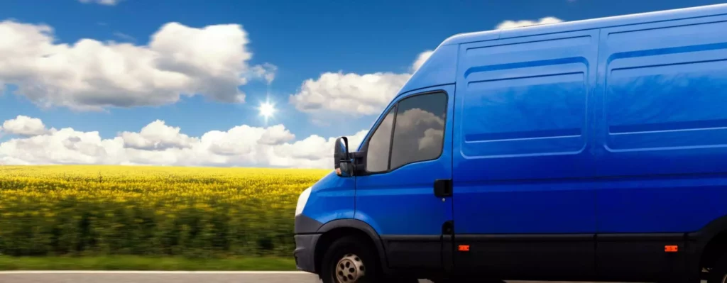 Blue delivery van driving past fields under a bright sky during a delay update Delays are inevitable, but how you handle them defines your reputation.