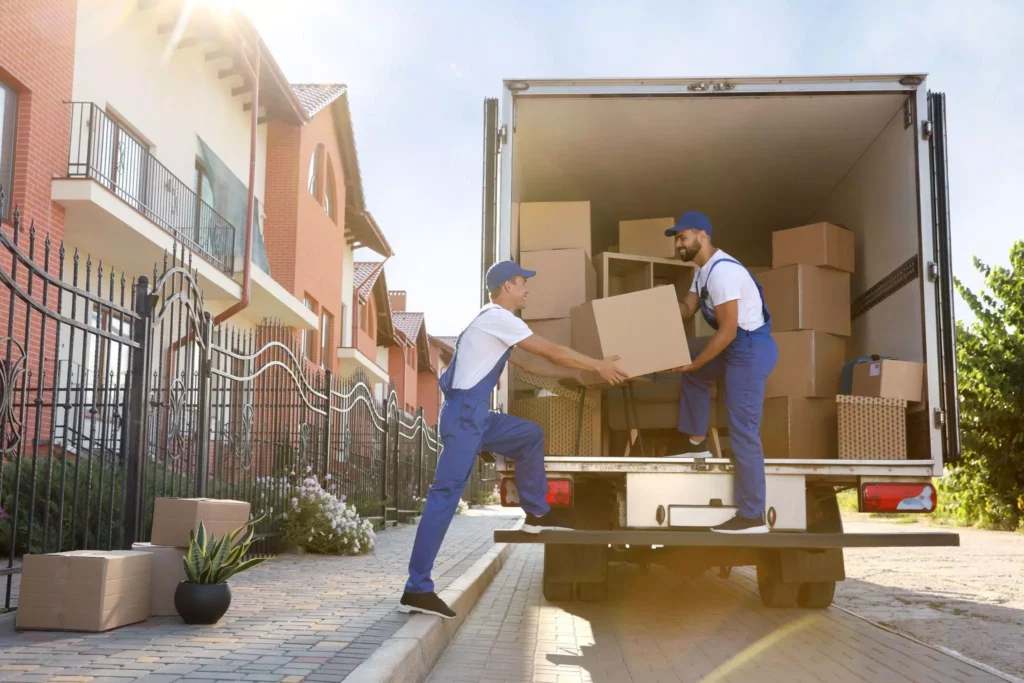 Two workers unloading packed boxes from a truck parked in a residential area