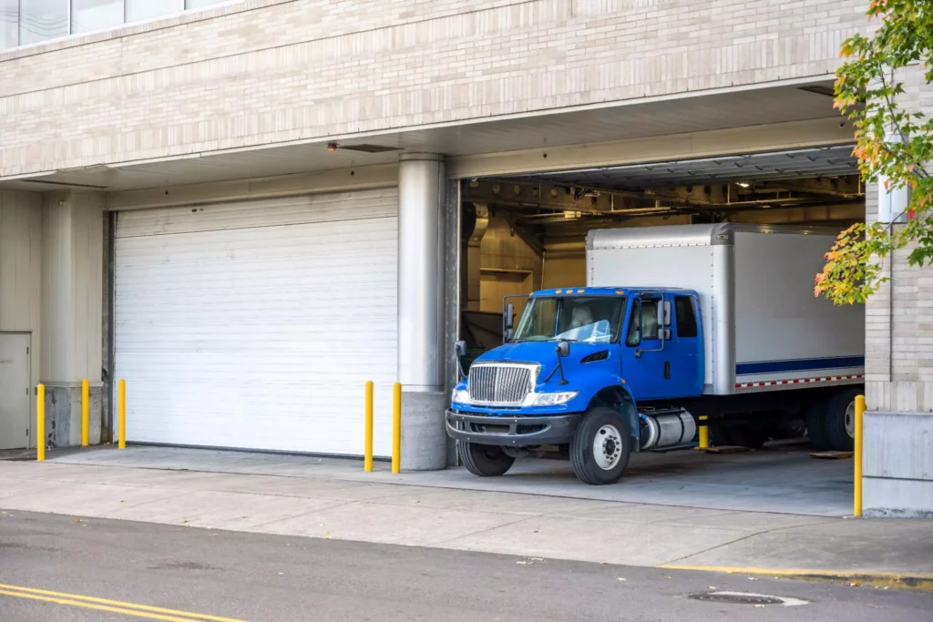 Large blue delivery truck parked in a warehouse loading dock entrance