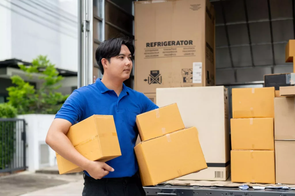 Worker holding multiple cardboard boxes while unloading items from a truck