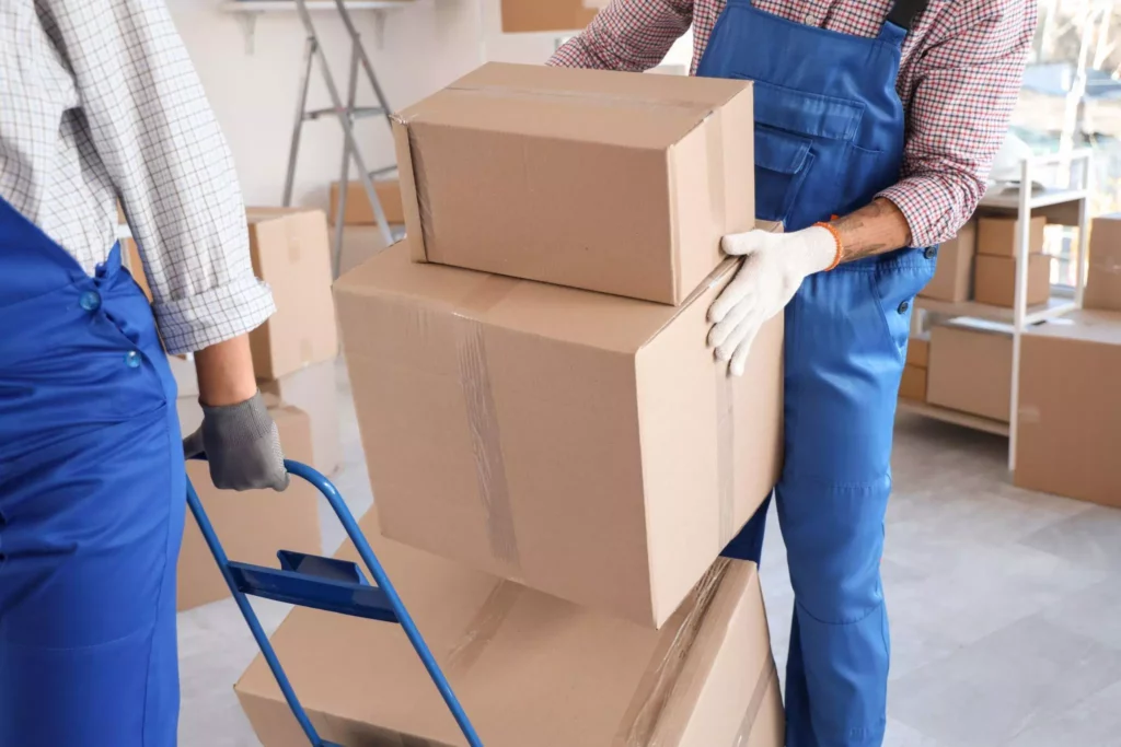 Workers stacking cardboard boxes on a hand truck indoors.