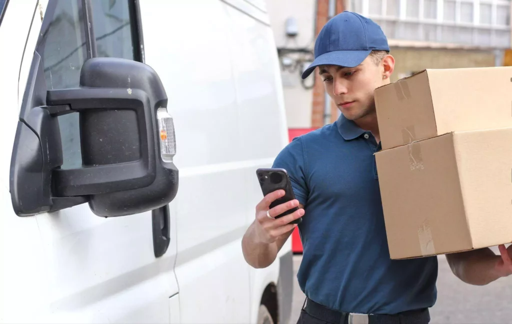 Delivery driver carrying parcels and checking mobile route app linked to Storis and NetSuite