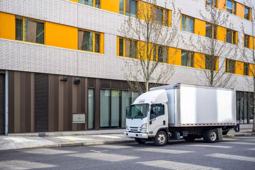 White box truck parked next to a modern building