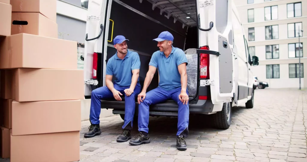 Two delivery drivers sitting at the back of a van surrounded by boxes, symbolizing teamwork and communication within a connected delivery platform.