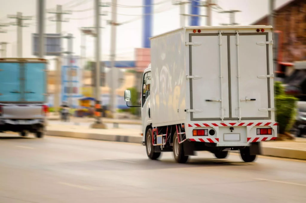 White box truck driving through a busy city street