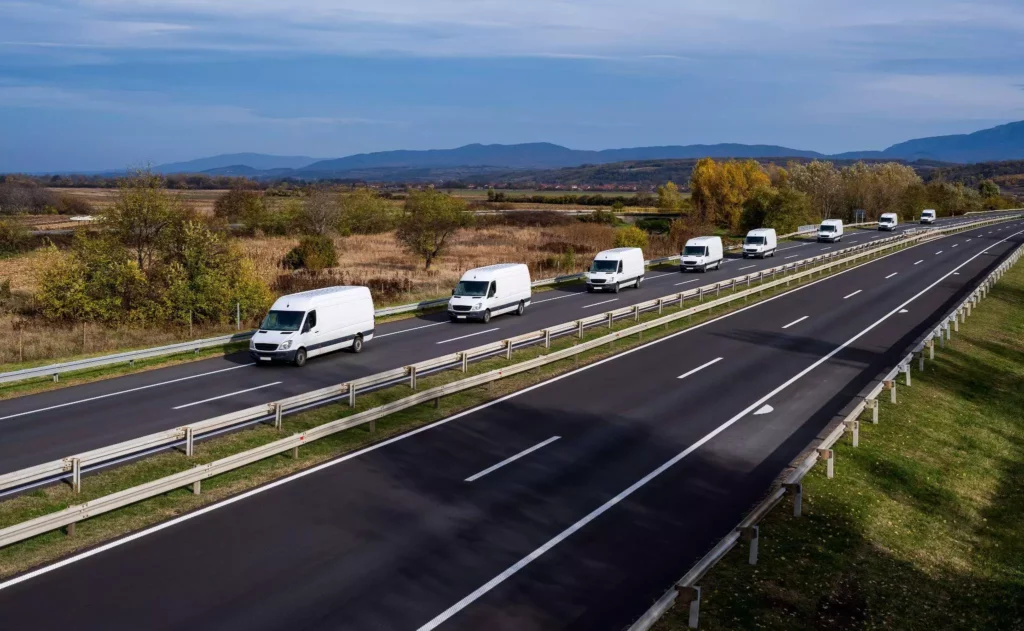 Convoy of white vans driving along a highway, representing coordinated fleet management and route density planning across integrated delivery systems
