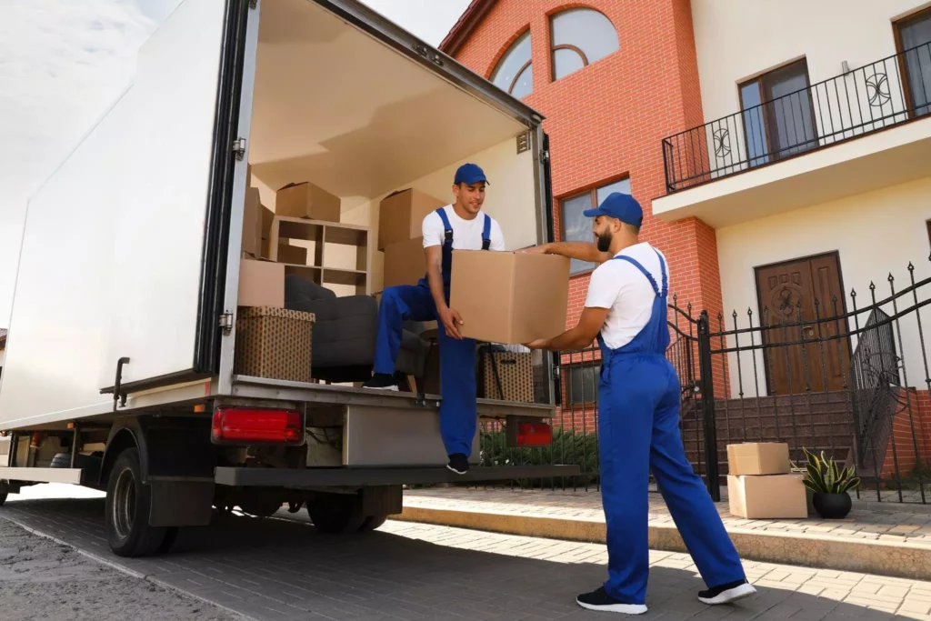Worker standing inside a truck handing a cardboard box down to another worker.