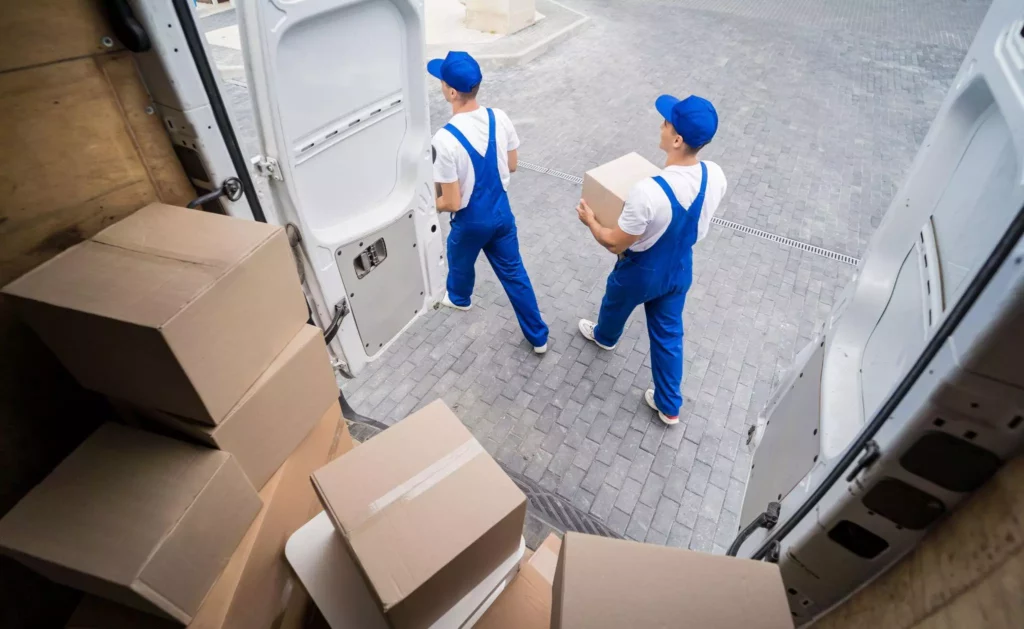 Two delivery workers in blue uniforms carrying boxes out of a van