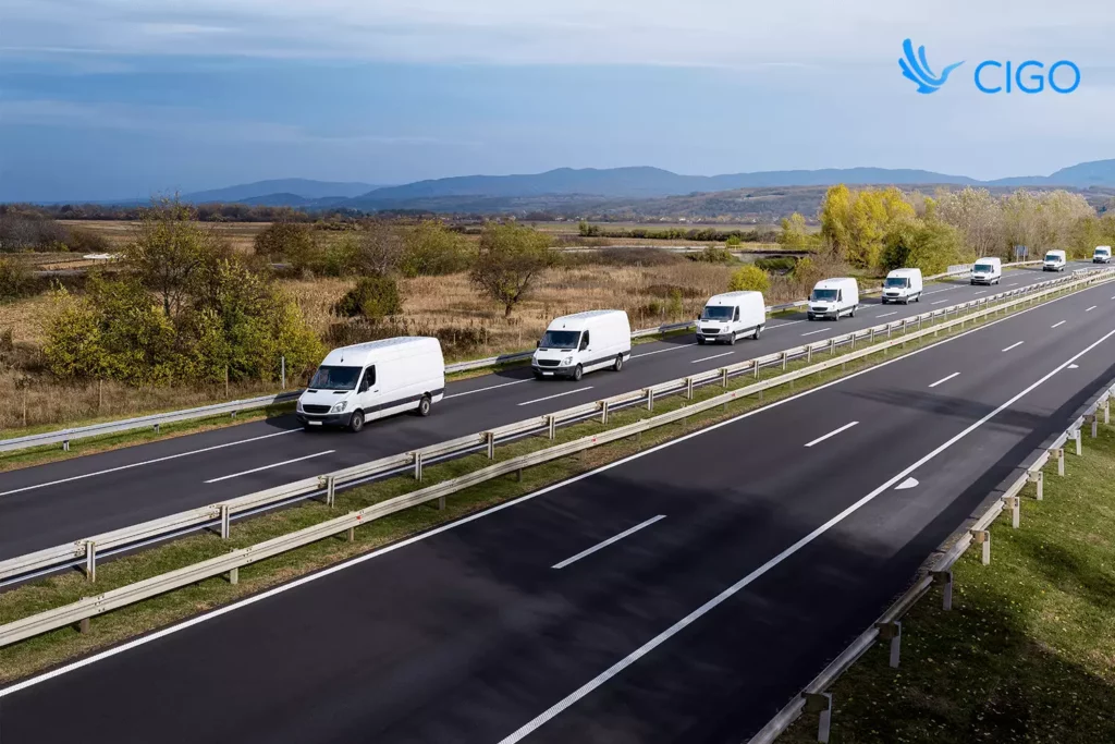 Convoy of white vans driving along a highway, representing coordinated fleet management and route density planning across integrated delivery systems.