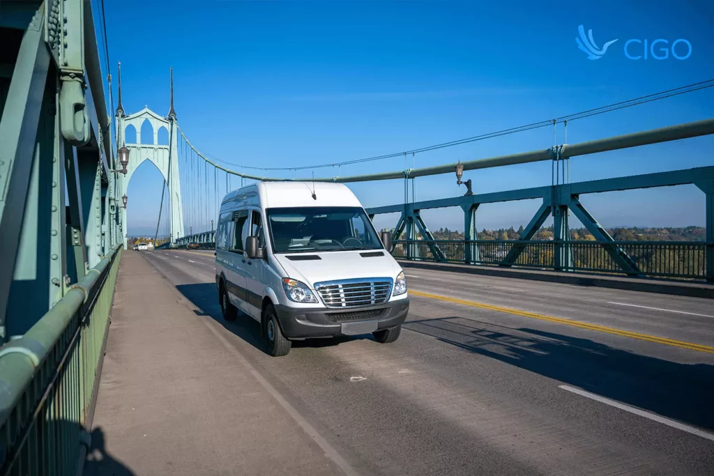 Delivery van crossing a steel bridge on a sunny day, symbolizing dynamic route optimization and ETA recalculations within connected delivery software