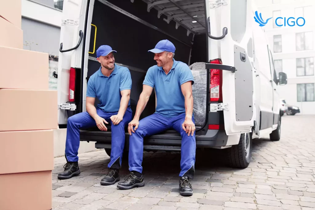 Two delivery drivers sitting at the back of a van surrounded by boxes, symbolizing teamwork and communication within a connected delivery platform.