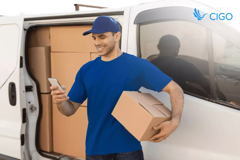 Courier holding a parcel and smiling at the phone with WooCommerce orders synced into the delivery app