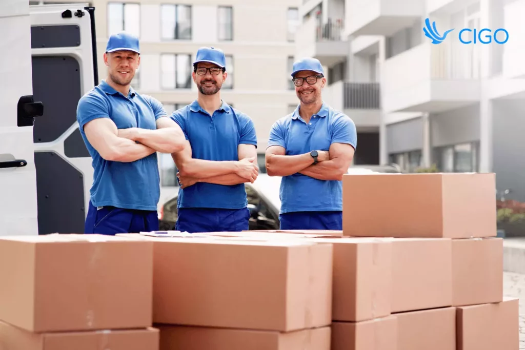 Three delivery workers in blue shirts standing by stacked boxes symbolizing integrated 3PL delivery teams