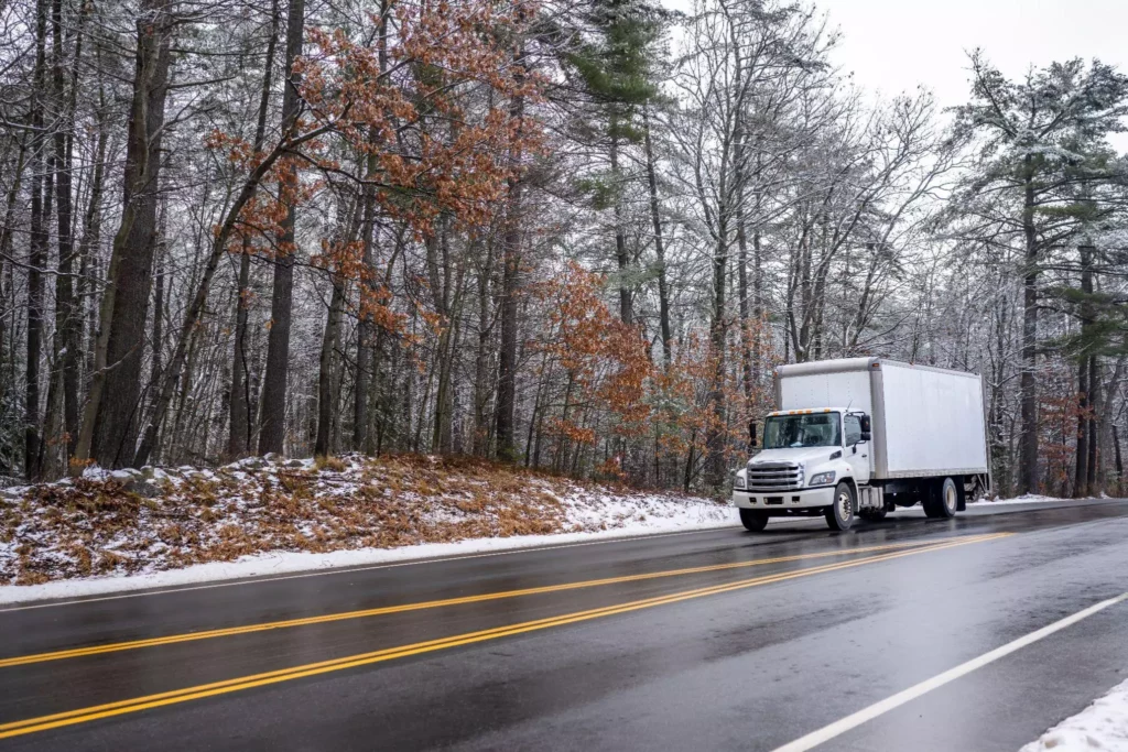 White box truck driving on a snowy forest road in winter