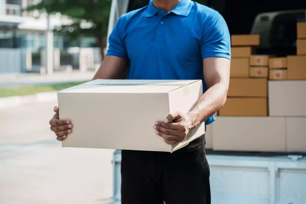 Delivery driver in blue uniform lifting a cardboard box from the van, representing efficient loading and fulfillment supported by delivery management software