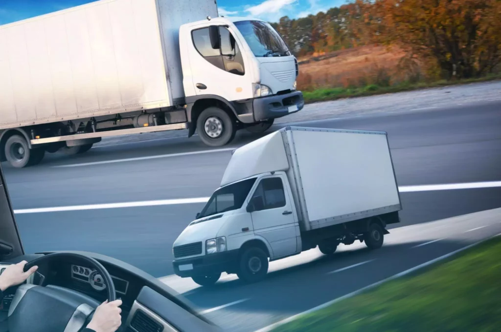 White box trucks driving on a multi-lane highway, viewed from inside another vehicle.