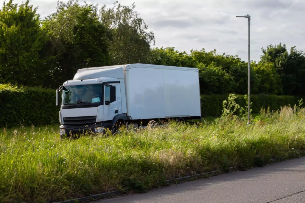 White delivery truck driving along a green suburban road, symbolizing optimized routing and fuel-efficient planning enabled by delivery management systems