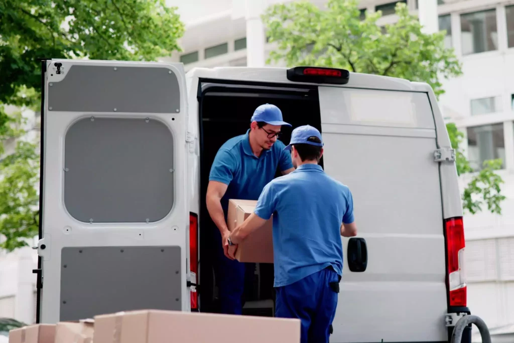 One worker stacks a pile of cardboard boxes while another reviews information on a tablet.
