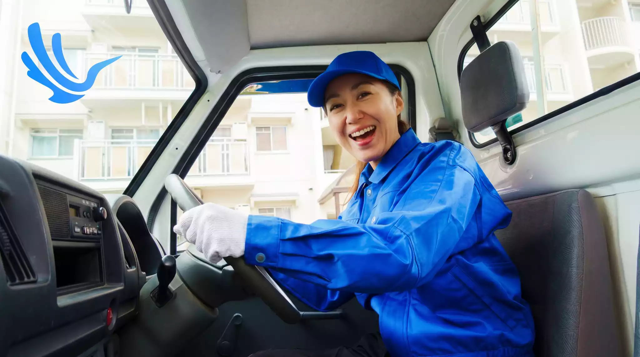 Female fleet driver smiling at wheel of delivery truck in urban zone