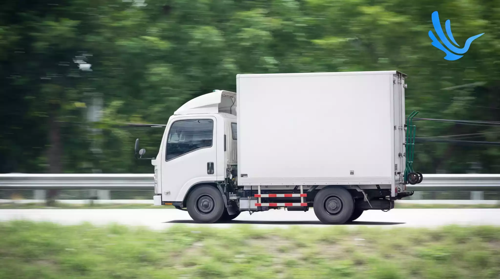 White box truck driving on highway through green landscape