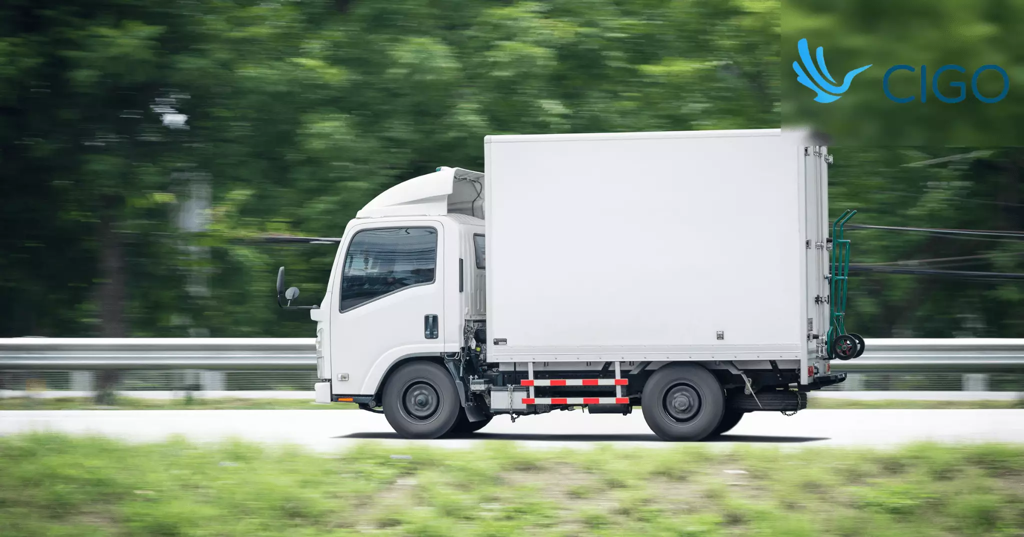 White box truck driving on highway through green landscape