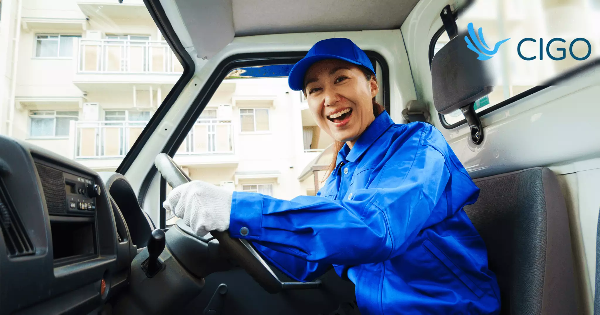 Female fleet driver smiling at wheel of delivery truck in urban zone