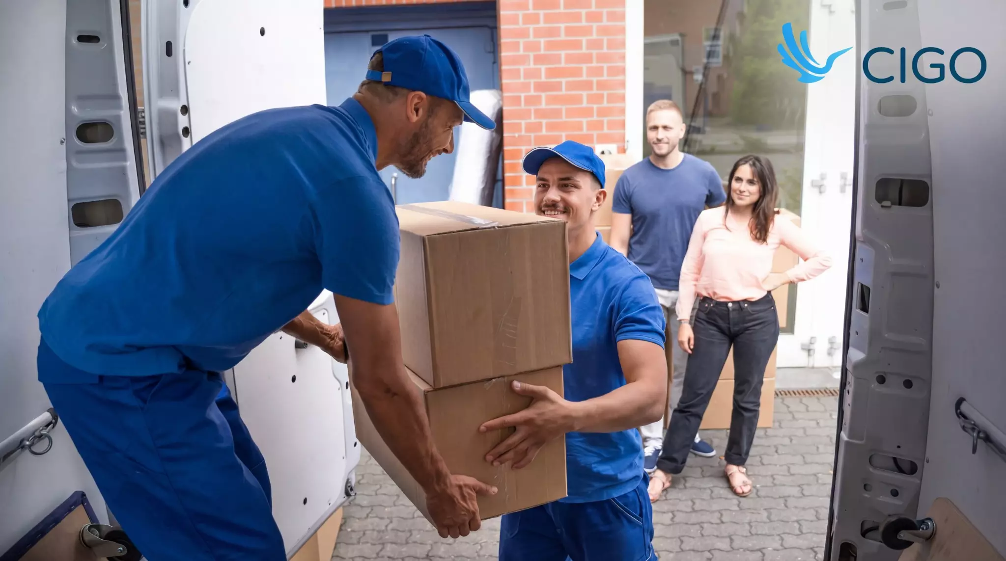 Two drivers hand off boxes at the delivery door while customers receive the order.